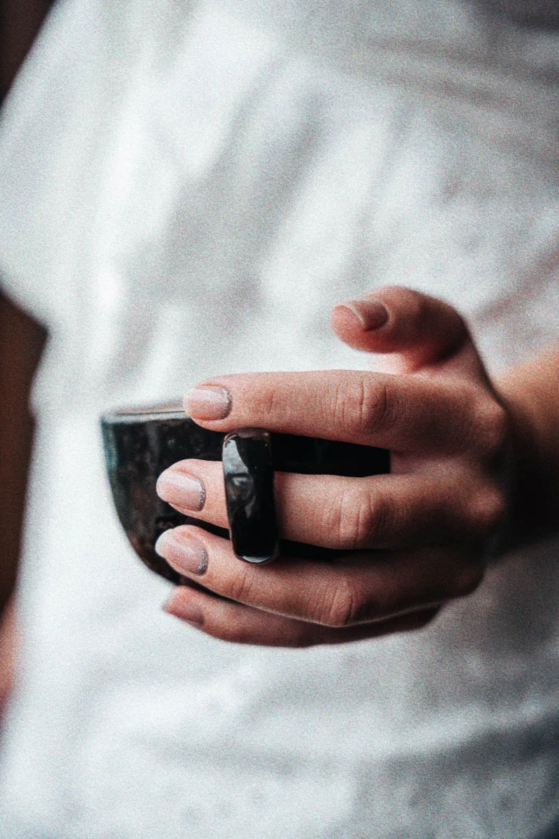 A close-up of manicured hands wrapped around a ceramic cup